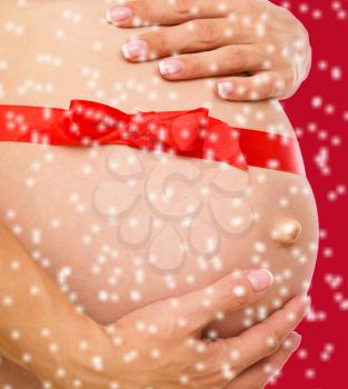 Image of pregnant woman touching her belly with hands, over red snowy background