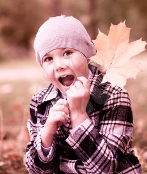 Cute little girl in autumn park hiding behind a tree