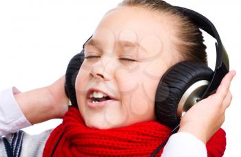 Cute little girl is enjoying music using headphones, isolated over white