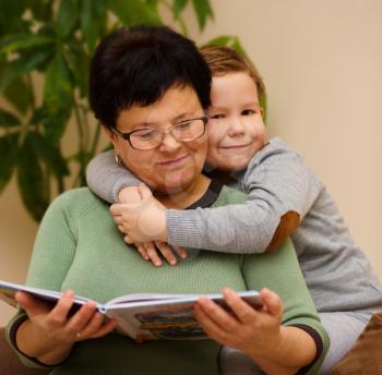 Grandmother is reading book with her grandson, indoor