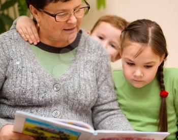 Grandmother is reading book with her grandchildren, indoors