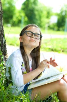 Cute little girl is reading a book outdoors