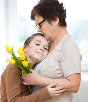 Happy grandmother with granddaughter. Woman and child with bouquet of flowers at home