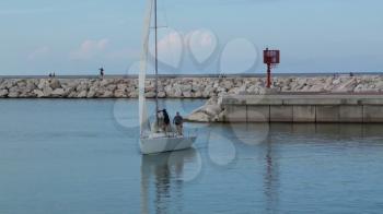 Sailing boat sails to the pier. The sailors lowered white sails.