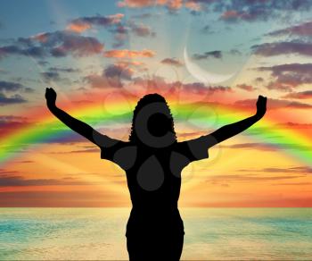 Happiness and success. Happy woman with raised arms on a rainbow background and sea sunset