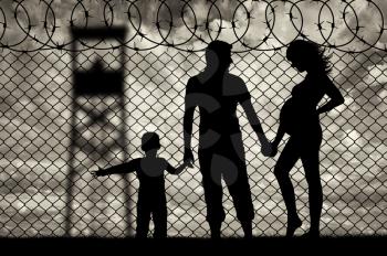 Refugees concept. Young refugee family with a child near the fence of barbed wire