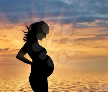 Pregnancy concept. Pregnant woman on a background of sea sunset