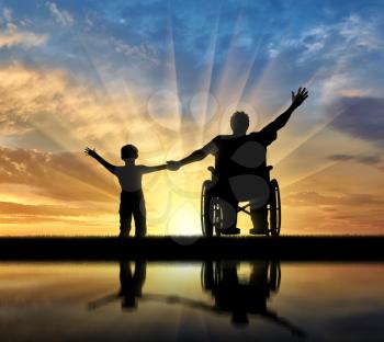 Happy disabled person in wheelchair hold son for hand and they happy and with their reflection in water on sunset. Concept happy disabled and familymily