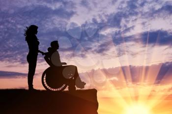 Concept of disability and disease. Silhouette of disabled person with a guardian on the hill in the evening
