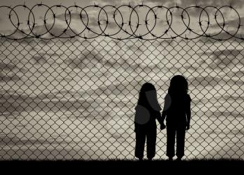 Concept of the refugees. Silhouette of hungry children in desperate refugees near the fence at sunset