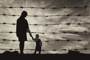 Concept of refugee. Silhouette of hungry refugees mother and child near the fence of barbed wire