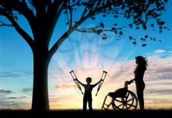 Happy disabled Child is invalid with crutches beside wheelchair and nurse near tree. Help concept