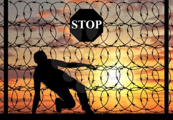 concept of the refugees. Silhouette of illegally crossing the border and refugee stop sign on a fence with barbed wire