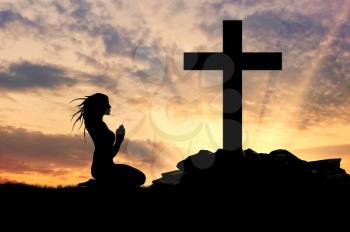 Concept of religion. Silhouette of a woman praying before the cross at sunset