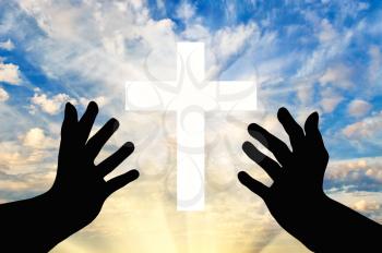 Concept of religion. Silhouette of praying hands and a cross against a beautiful sky