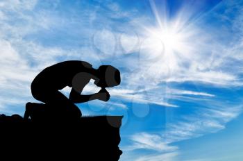 Silhouette of man praying at the top against the beautiful cloudy sky
