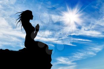 Silhouette of praying woman on top against cloudy sky