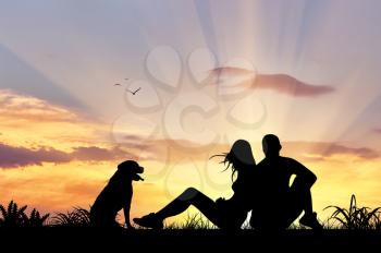 Silhouette of man and woman sitting with a dog admiring the sunset