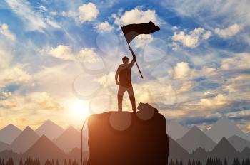 Silhouette of a climber on a mountain top with a flag in his hand. success concept