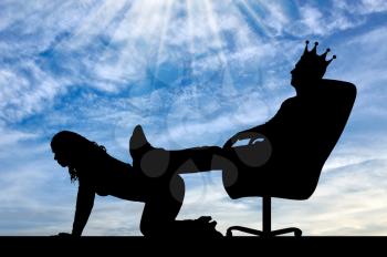 Silhouette of a selfish man with a crown on his head sitting in a chair, threw back his legs on the woman's back. The concept of discrimination and inequality to women