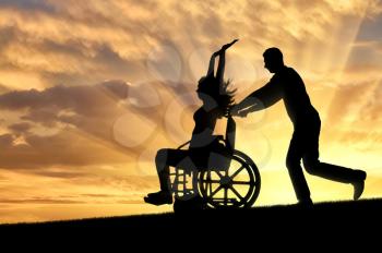 A disabled woman in a wheelchair is having fun with a man at sunset. The concept of the way of life of people with disabilities