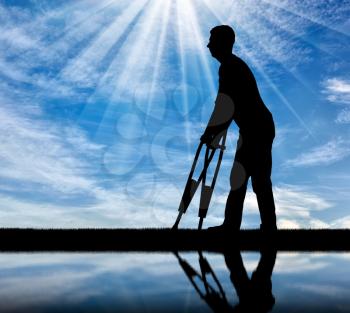 Silhouette of a disabled man with crutches walking near the river with his reflection. Concept of people with disabilities
