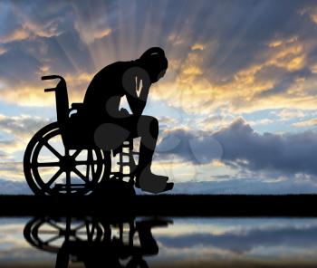 Silhouette of a sad disabled woman in a wheelchair by the river with her reflection. The concept of people with disabilities experiencing grief and sadness