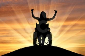 Silhouette of a happy disabled woman in a wheelchair on top of a hill. The concept of happy people with disabilities