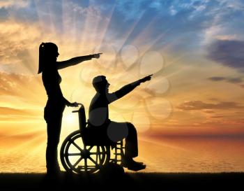 Silhouette of a disabled man in a wheelchair and his wife have a good time by the sea. The concept of caring and supporting disabled people in the family