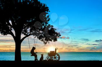 Girl schoolgirl invalid sitting on a swing under a tree by the sea, reading a book, beside a wheelchair and her dog. Concept of children with disabilities