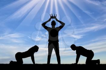 Silhouette of a man and a woman worshiping a man who puts a crown on his head. The concept of a selfish and arrogant person
