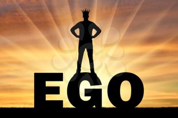 Silhouette of a man with a crown on his head standing on the word ego against the backdrop of a sunset. Concept of selfishness