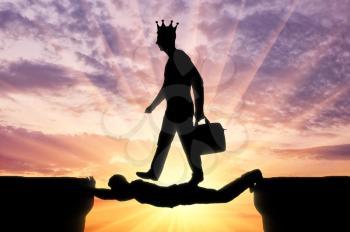 Selfish man with a crown on his head is walking over a man in the form of a bridge over an abyss. The concept of selfishness