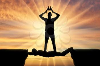 Selfish man puts a crown on his head, he stands on a man in the form of a bridge over a precipice. Concept of selfishness
