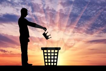 Silhouette of a man throws a crown in the garbage bin. The concept of selfishness as a bad habit from which it is necessary to refuse