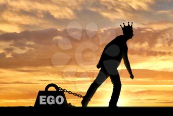A big weight in the form of an ego is chained to the foot of a selfish and narcissistic man with a crown on his head. The concept of egoism as a problem interfering with living a full life