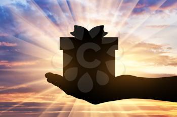 Altruism concept. Silhouette of a hand giving a gift on a sunset background