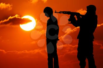 Silhouette of man with rifle pointed at victim's back