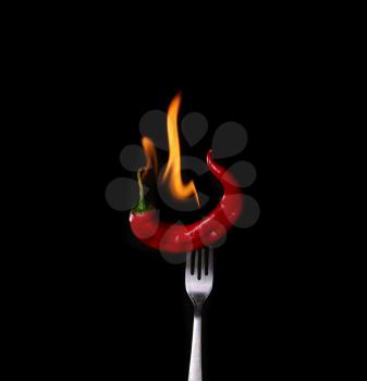Fork impale to red hot chili on black background.