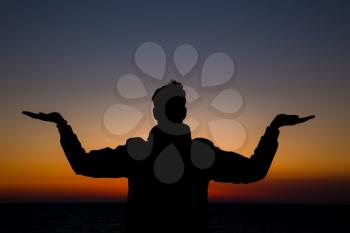 Silhouette of a man practicing yoga on a grassy horizon after sunset. Silhouette against a bright orange sky.