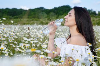 Beautiful woman on a flower granden enjoying her time outdoors. pretty girl relaxing outdoor, having fun, holding plant, drinking water from a small bottle