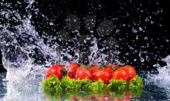 Fresh tomato cherry and green fresh salad with water drop splash on dark background Macro drops of water fall on the red cherry tomatoes and make splash