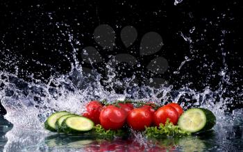 Studio shot with freeze motion of cherry tomatoes and slices of cucumber in water splash on black background