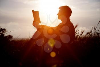 Man reading in the park against sunset. Silhouette of man reading book at sky sunset . warm tone and soft focus