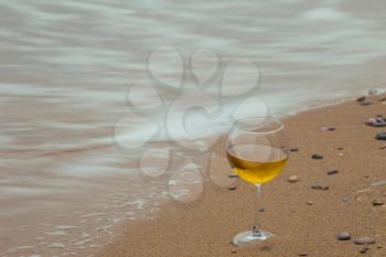 Romantic glass of wine sitting on the beach, overcast autumn weather, cold wind