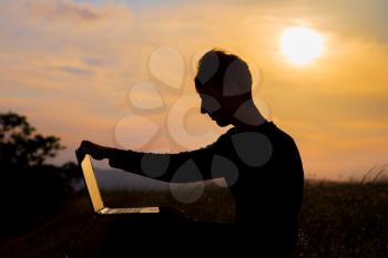 silhouette of happy business man with laptop working on the field at sunset time