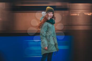 Beautiful winter portrait of young woman in the winter snowy scenery. Pretty red-haired girl walking on a winter evening city