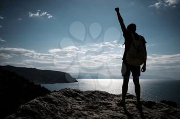 Hiker with backpack standing on top of a mountain with raised hands and enjoying view