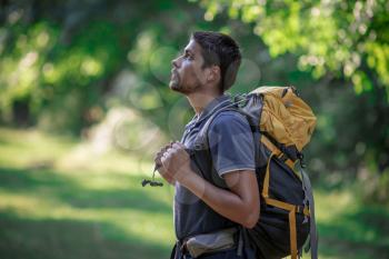 Young smiling backpack man in summer forest nature. Happy handsome male adult student looking at camera walking hiking in forest background. School bag or backpacking travel concept.