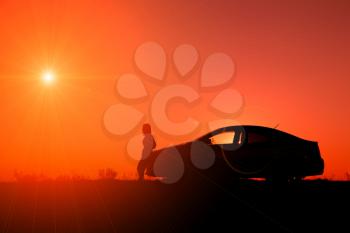 Young girl with and broken car. Silhouette of sedan car with girl on the background of beautiful sunset